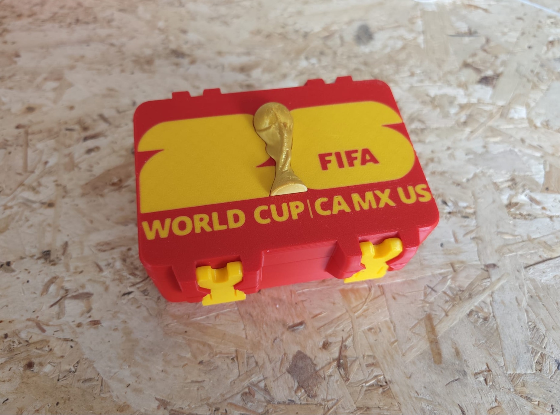 Caja_Mundial FIFA Caja para cromos del Mundial de fútbol roja y amarilla sobre mesa de madera